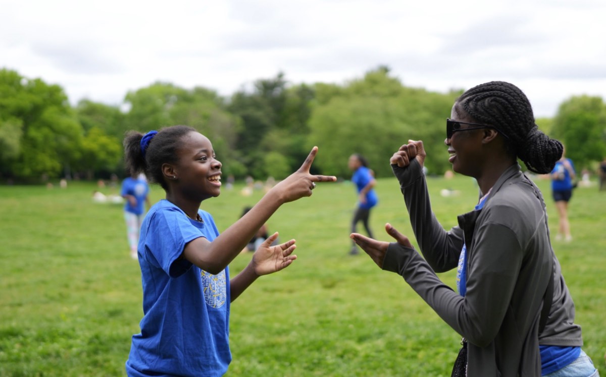 A young participant and a youth mentor laughing together during a warm-up game in Prospect Park